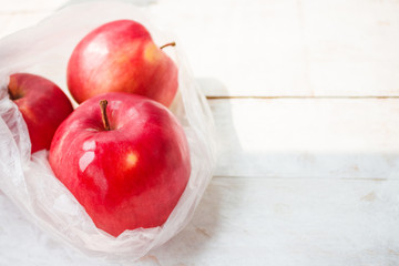 ripe organic apples in plastic bag on wooden background copy space