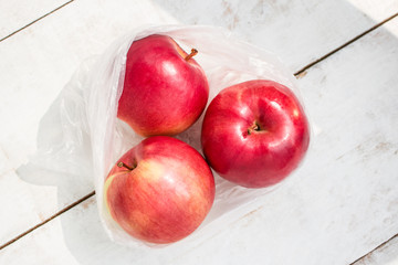 three fresh apples in plastic bag on white wooden table top view