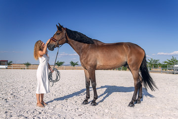 blonde girl with white dress stroking a horse