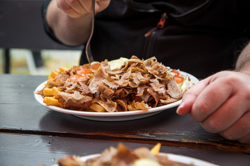 Mann isst Döner Kebab Teller mit Pommes, Salat, Scharf und Knoblauch Sauce