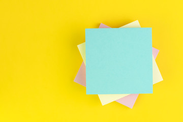 Stack of sticky notes on solid yellow background with pink, yellow and blue on top with copy space for writing message using as memo, reminder or record idea