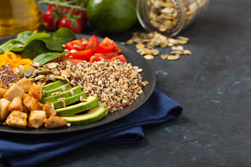 Salad with quinoa, avocado and chicken. Front view. Served on a black plate.