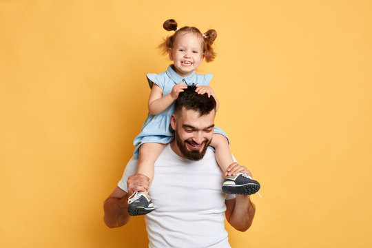 positive cheerful daddy playing with daughter, entertaining her, close up photo. isolated yellow background