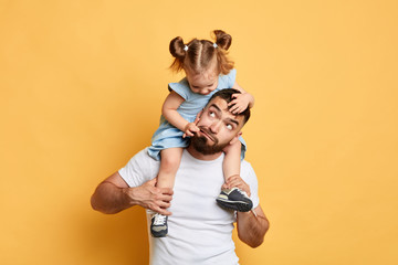 naughty girl throwing a tantrum, doing confusing things, kid pulling her dad's face, skin, making fun of elder brother, mocking her dad. close up photo. isolated yellow background - 280889337