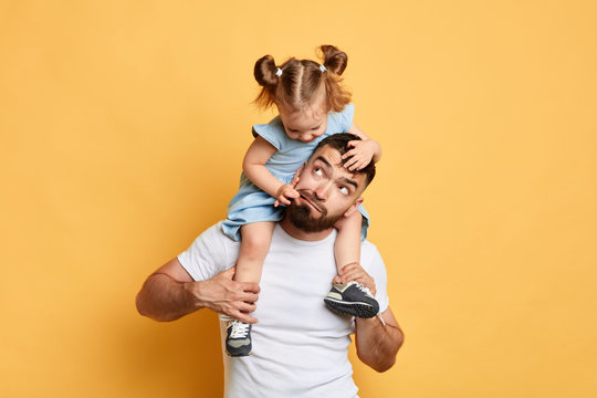 naughty girl throwing a tantrum, doing confusing things, kid pulling her dad's face, skin, making fun of elder brother, mocking her dad. close up photo. isolated yellow background
