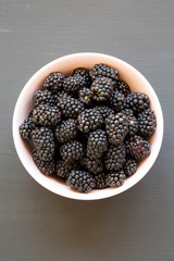 Blackberries in a pink bowl over black surface, top view. Summer berry. From above, overhead. Close-up.