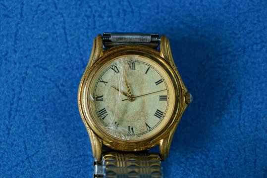 yellow old wrist watch with broken glass on a blue table