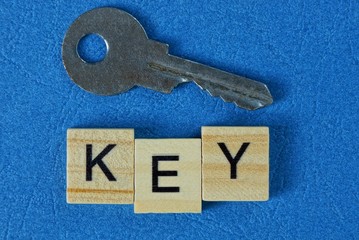 one gray metal door key and the inscription of wooden letters on a blue table