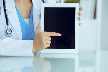 Female doctor using tablet computer while sitting at the workplace, close-up of hands. Medicine, healthcare and help concept