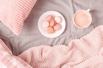Bed with pink knitted plaid, coffee and macaroons.