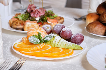 fruit sliced on a white plate of pears, tangerines, oranges and grapes dusted with icing sugar.