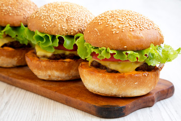 Homemade cheeseburgers on a rustic wooden board, side view. Close-up.