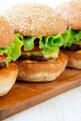Homemade cheeseburgers on a rustic wooden board, side view. Closeup.
