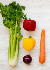 Fresh vegetables (carrot, celery, onion, colored peppers) on a white wooden background, top view. From above, overhead, flat lay.
