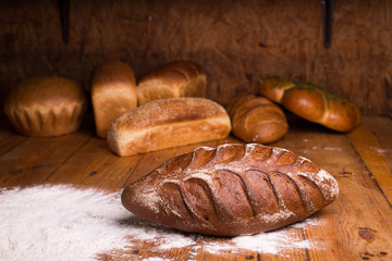 Whole grain black bread with bran on a wooden table with different breads on the background. Loaf of bread with flour on a dark background