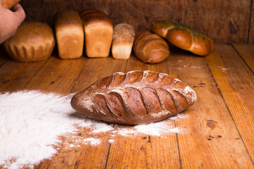 Whole grain black bread with bran on a wooden table with different breads on the background. Loaf of bread with flour on a dark background