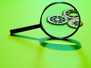 Magnifying glass on a green surface with gears in the background 