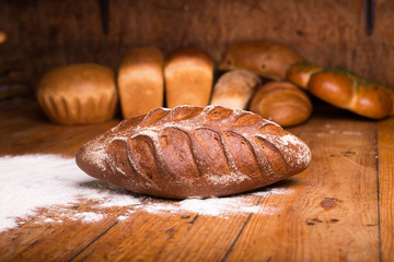 Whole grain black bread with bran on a wooden table with different breads on the background. Loaf of bread with flour on a dark background