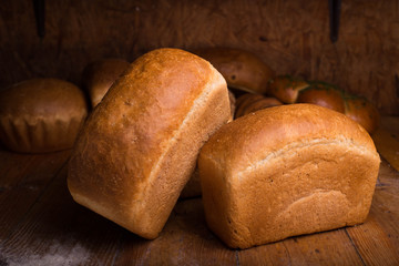 Two loaves of bread on a wooden table with different breads on the background. Baking on a dark background