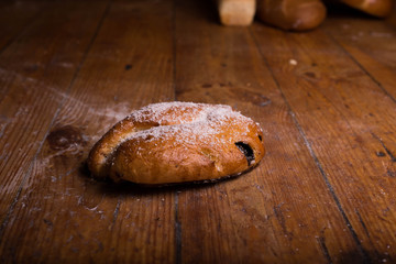 Sweet bun on the wooden table. Small cherry pie sprinkled with coconut chips.