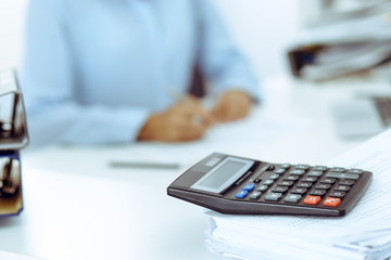 Calculator and binders with papers are waiting to be processed by business woman or bookkeeper back in blur. Internal Audit and tax concept