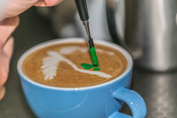 Barista making an art from the fresh milk in the little ceramic cup of the delicious hot espresso