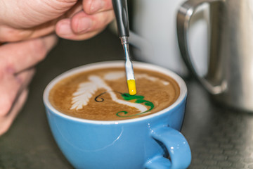 Barista making an art from the fresh milk in the little ceramic cup of the delicious hot espresso