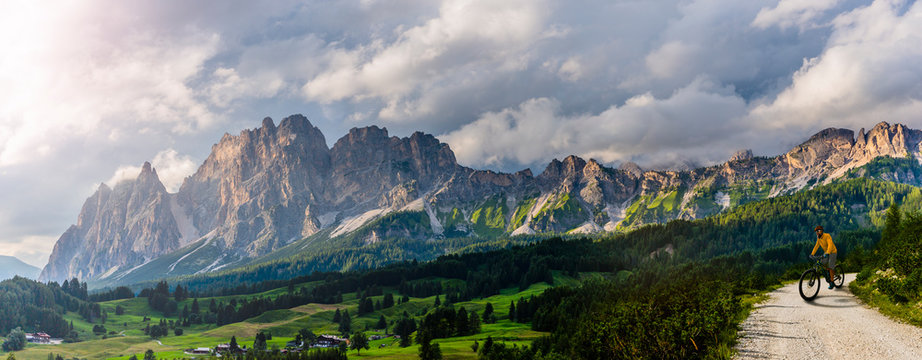 Tourist cycling in Cortina d'Ampezzo, stunning rocky mountains on the background. Man riding MTB enduro flow trail. South Tyrol province of Italy, Dolomites.