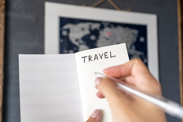 Female hands holding notebook and pen, making notes when planning a travel route and expenses in front of the map of the world. Close-up