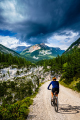 Fototapeta na wymiar Tourist cycling in Cortina d'Ampezzo, stunning rocky mountains on the background. Woman riding MTB enduro flow trail. South Tyrol province of Italy, Dolomites.