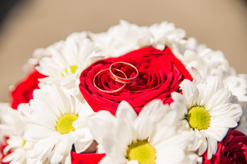 Obraz na płótnie Canvas Wedding rings are on the bride's bouquet. Wedding bouquet of white daisies and red roses. Wedding background for cards and invitations.