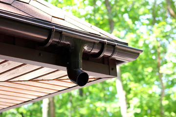 Modern roof of house with plastic rain gutter on beautiful natural background with green vegetation