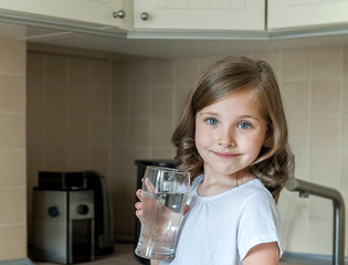 Little child is drinking clean water at home, close up. Caucasian cute girl with long hair is...
