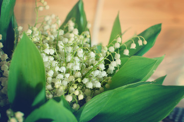 A bouquet of delicate white lilies of the valley surrounded by green leaves on the table