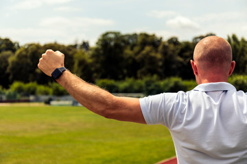 Fototapeta premium Strong bald men points to something in football field. Back view of handsome man in t-shirt pointing.