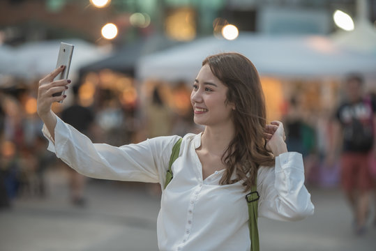 Happy Asian teenager selfie herself with smartphone during travel on night market.