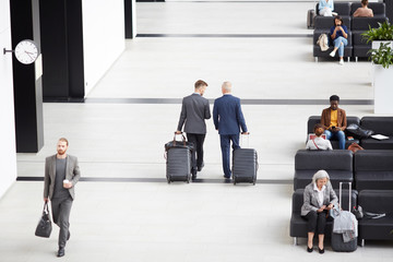 Above view of modern businessmen in formalwear carrying wheeled suitcases while crossing airport...