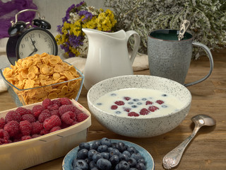 Breakfast.Corn sticks ,and cereal with milk.Raspberries and blueberries.On the background colors