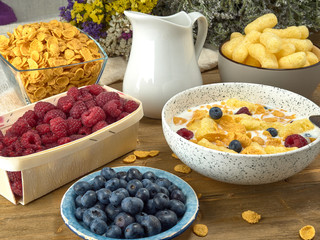 Breakfast.Corn sticks ,and cereal with milk.Raspberries and blueberries.On the background colors