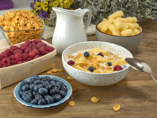 Breakfast.Corn sticks ,and cereal with milk.Raspberries and blueberries.On the background colors