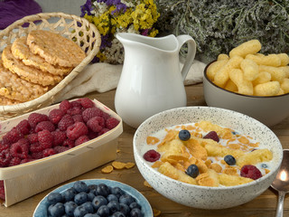 Breakfast.Corn sticks ,and cereal with milk.Raspberries and blueberries.On the background colors