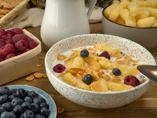 Breakfast.Corn sticks ,and cereal with milk.Raspberries and blueberries.On the background colors