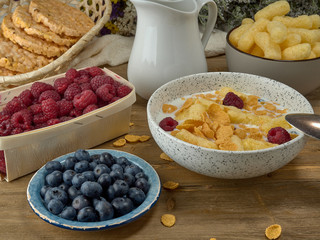 Breakfast.Corn sticks ,and cereal with milk.Raspberries and blueberries.On the background colors