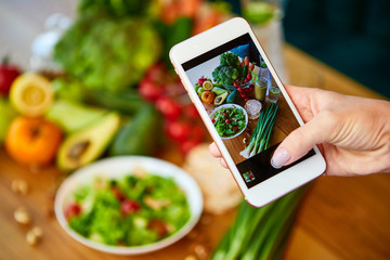 Woman hands take smartphone food photo of vegetables salad with tomatoes and fruits. Phone photography for social media or blogging. Vegan lunch, vegetarian dinner, healthy diet