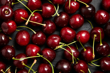 Cherries background. Red ripe berries scattered on a black table