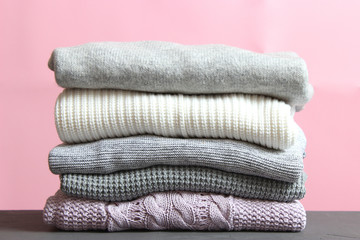 A pile of warm sweaters on a wooden table on a color background. Autumn and winter clothes.