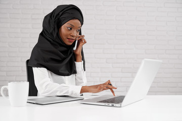 African muslim woman working in call centre, using laptop.