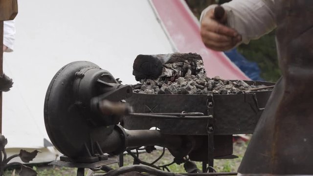 Blacksmith turning handle of hand-cranked blower to push air to forge. Slavic and old culture days in Sobotka, Poland.