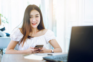 Portrait of young asian woman using smartphone and laptop working n cafe