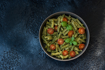 Fusilli pasta with green pesto sauce on a black concrete background. traditional Italian dish. Copy space
